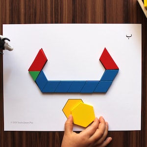 Peut inclure: Une main d'enfant tient une forme hexagonale jaune au-dessus d'une feuille de papier blanche. Le papier présente une forme géométrique bleue, verte et rouge qui forme la lettre arabe "Ba". La lettre "Ba" est écrite en noir sur un cercle en bois dans le coin supérieur droit de l'image. Le texte "Teach Quran Play" est écrit dans un cercle coloré dans le coin inférieur droit de l'image.