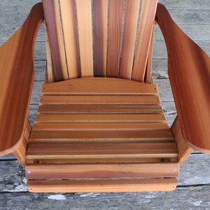 May include: A wooden adirondack chair with a natural wood finish. The chair has a slatted back and seat, and wide armrests.