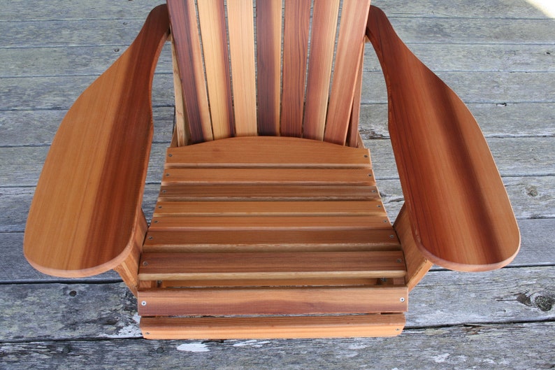 May include: A wooden adirondack chair with a natural wood finish. The chair has a slatted back and seat, and wide armrests.