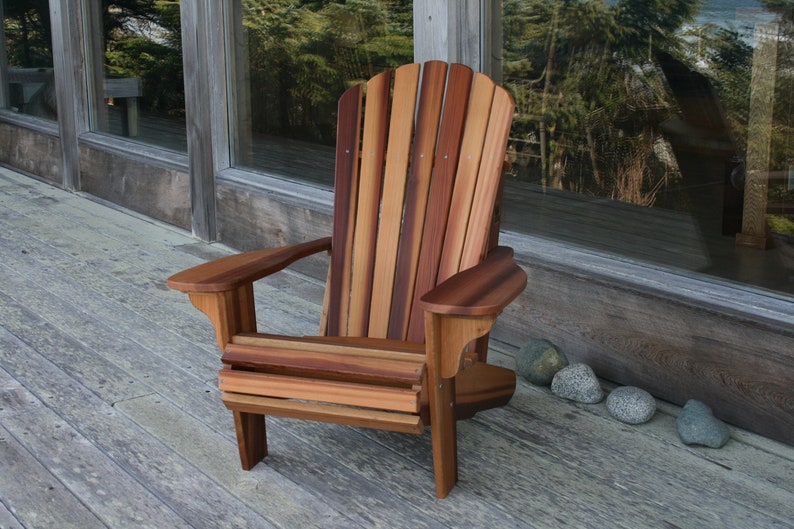 May include: A wooden adirondack chair with a natural wood finish. The chair is made of cedar wood and has a slatted back and seat. The chair is sitting on a wooden deck.