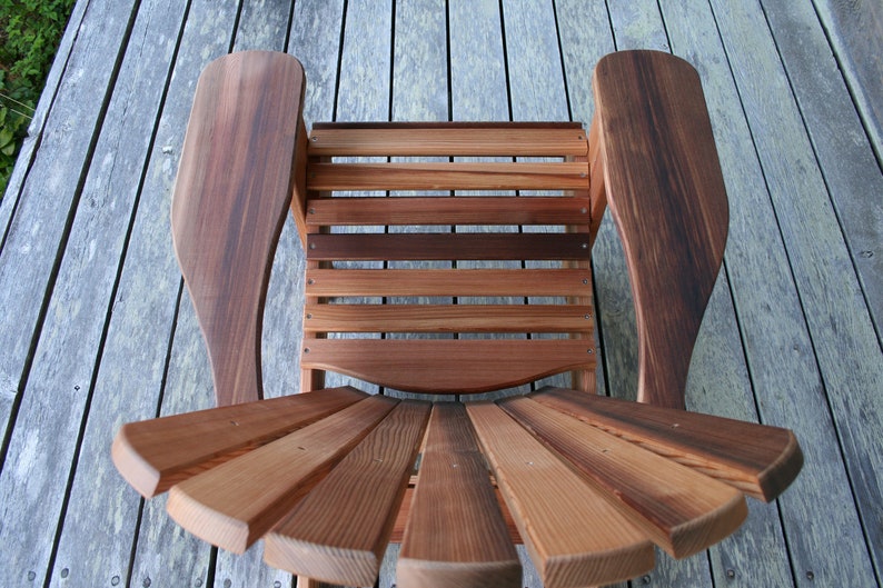 May include: A wooden chair with a slatted back and seat, and curved armrests. The chair is made of natural wood with a reddish-brown color.