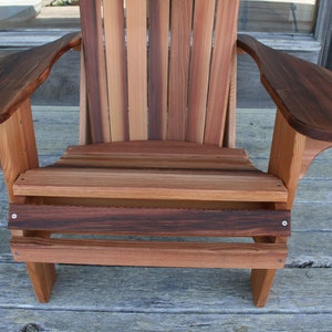 May include: A wooden adirondack chair with a natural wood finish. The chair has a wide, comfortable seat and armrests. The chair is made of solid wood and is designed for outdoor use.