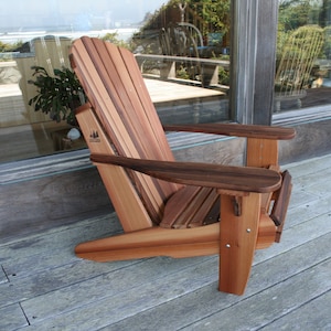 May include: A wooden adirondack chair with a natural wood finish. The chair is made of cedar and has a wide, comfortable seat and back. The chair is sitting on a wooden deck.