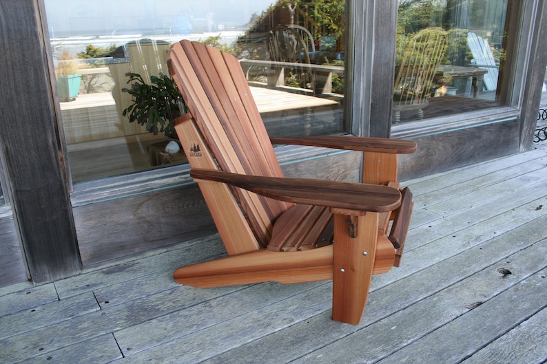 May include: A wooden adirondack chair with a natural wood finish. The chair is made of cedar and has a wide, comfortable seat and back. The chair is sitting on a wooden deck.