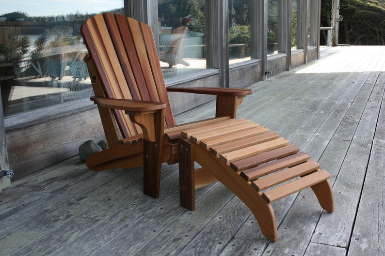 May include: A wooden adirondack chair with a matching footrest. The chair and footrest are made of natural wood with a reddish-brown color.