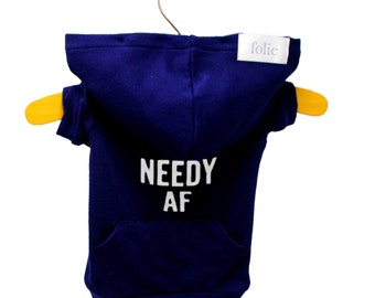 Puede incluir: Una sudadera con capucha azul marino para un perro pequeño con el texto "NEEDY AF" impreso en blanco en la espalda. La sudadera tiene un bolsillo en la parte delantera y una etiqueta blanca con la palabra "folie" en el hombro derecho.