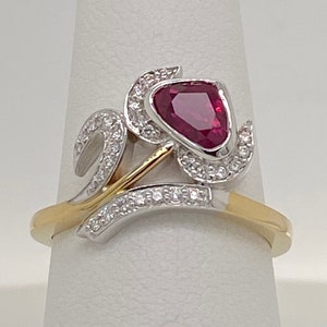 May include: A gold and silver ring with a red gemstone and small diamonds set in a floral design.