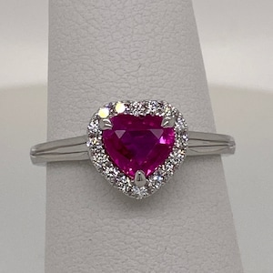 May include: A heart-shaped pink gemstone ring with a halo of smaller diamonds set in a silver band.