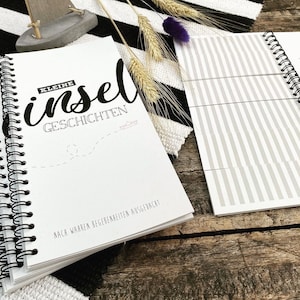 Può includere: Un quaderno a spirale bianco con il testo "KLEINE insel GESCHICHTEN" e le parole "NACA WARREN BEGEBENBEITEN AUSGEDACAT" sulla copertina.