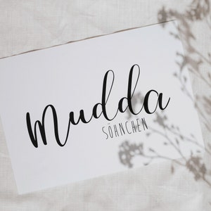 May include: White card with black calligraphy that reads "mudda" and "söhnchen" in a cursive font.