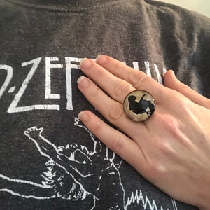 May include: A ring with a round, beige and black cameo featuring a silhouette of a person. The cameo is set in a silver ring.