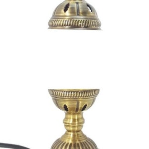 Może przedstawiać: Złota metalowa lampa stołowa z ozdobnym wierzchołkiem i okrągłą podstawą. Lampa ma przewód i wtyczkę.