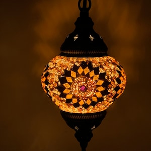 May include: A round, mosaic glass pendant light with a gold and brown pattern and a purple centre. The light is hanging from a black chain.