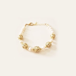 May include: A gold and white bracelet with a delicate chain and round, ornate gold beads.