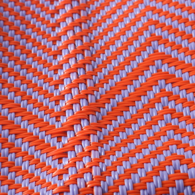 May include: Close-up of a woven plastic mat with a checkered pattern in orange and purple.