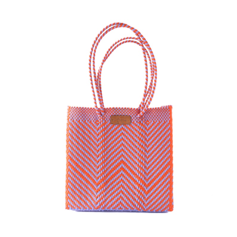 May include: A woven tote bag with a chevron pattern in orange and purple. The bag has two handles and a small leather tag.