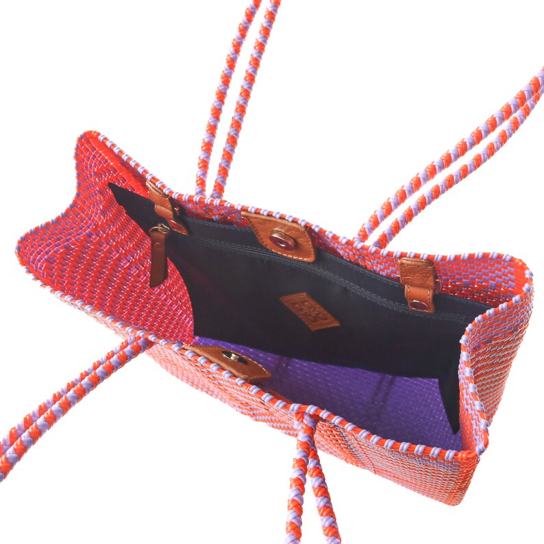 May include: A woven tote bag with orange and purple stripes. The bag has two long handles and a zippered pocket on the inside. The bag is open and the inside is visible.