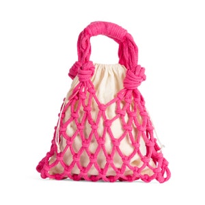 May include: A bright pink macrame tote bag with a cream-colored drawstring pouch inside. The bag features a woven net design and a thick, knotted handle. The bag is designed to be carried by hand.