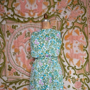 May include: A sleeveless dress with a floral print in shades of blue, green, and purple. The dress has a fitted bodice and a slightly flared skirt. It is belted at the waist.