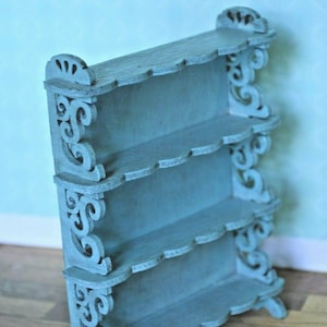 May include: A light blue wooden shelf unit with intricate scrollwork details and four shelves. The shelf unit is freestanding and has a decorative scalloped edge.