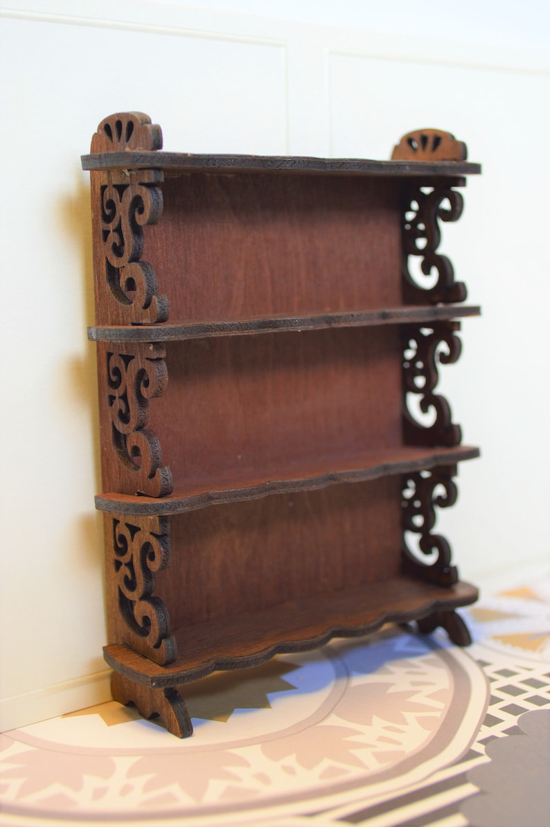 Pu&ograve; includere: Un'unit&agrave; a scaffale in legno con tre ripiani e decorazioni a volute sui lati. L'unit&agrave; a scaffale &egrave; di colore marrone e ha un aspetto rustico.