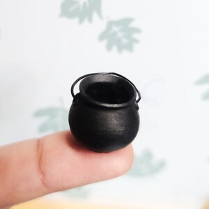 Op de afbeelding: Een kleine zwarte ketel met een handvat, liggend op een vinger.