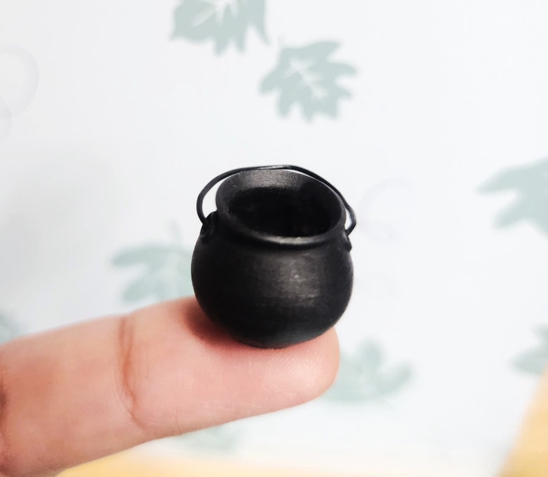 Op de afbeelding: Een kleine zwarte ketel met een handvat, liggend op een vinger.