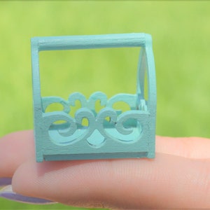 May include: A small, light blue wooden crate with decorative cutouts. The crate has a handle on top and is made of thin wood.