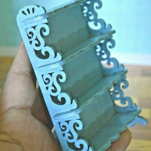 May include: A light blue wooden shelf unit with intricate scrollwork details. The shelf has four tiers and is designed for miniature items.