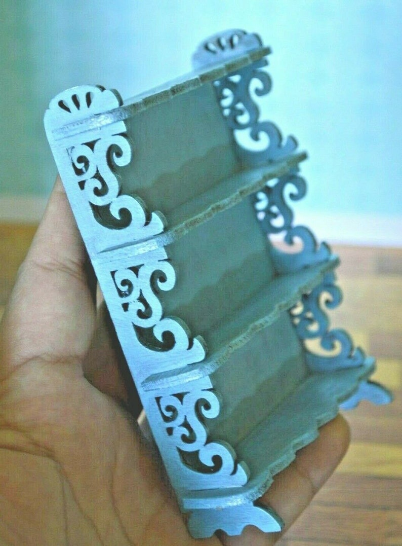 May include: A light blue wooden shelf unit with intricate scrollwork details. The shelf has four tiers and is designed for miniature items.
