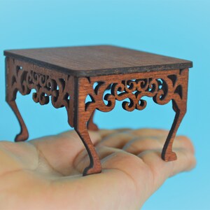 May include: A miniature wooden table with intricate carved details and four legs. The table is made of dark brown wood and has a rectangular top.