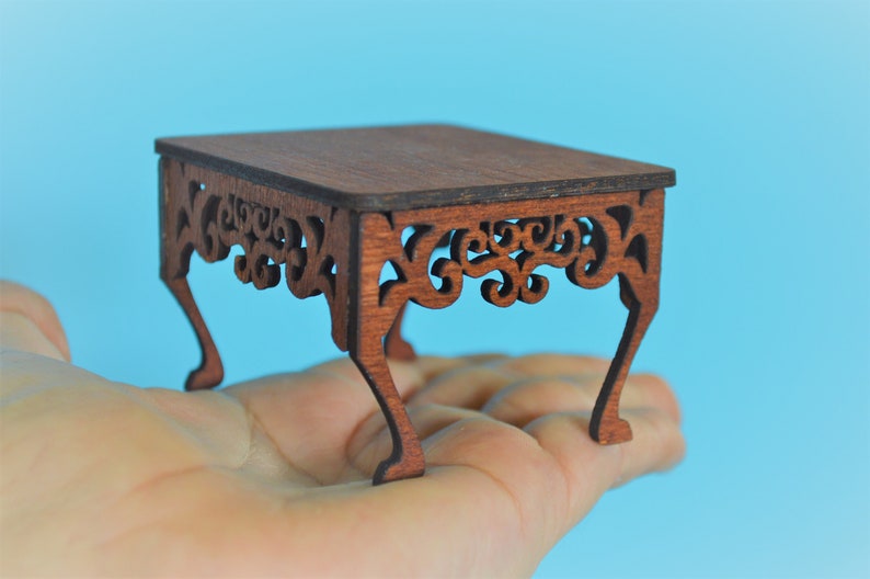 May include: A miniature wooden table with intricate carved details and four legs. The table is made of dark brown wood and has a rectangular top.