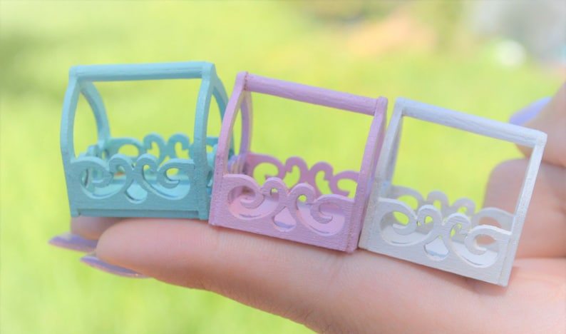 May include: Three miniature decorative baskets in pastel colors. The baskets are made of wood and have a cutout design. The baskets are painted in light blue, pink, and white.