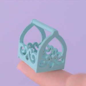 May include: A small, light blue wooden basket with a decorative, ornate design. The basket has a handle and is perfect for holding small items.
