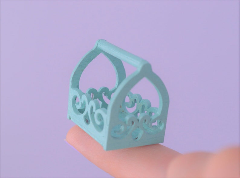 May include: A small, light blue wooden basket with a decorative, ornate design. The basket has a handle and is perfect for holding small items.