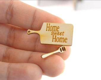 Puede incluir: Una pequeña tabla de cortar de madera con el texto "Home sweet Home" grabado en ella. También se incluye una pequeña cuchara de madera con un diseño ranurado.