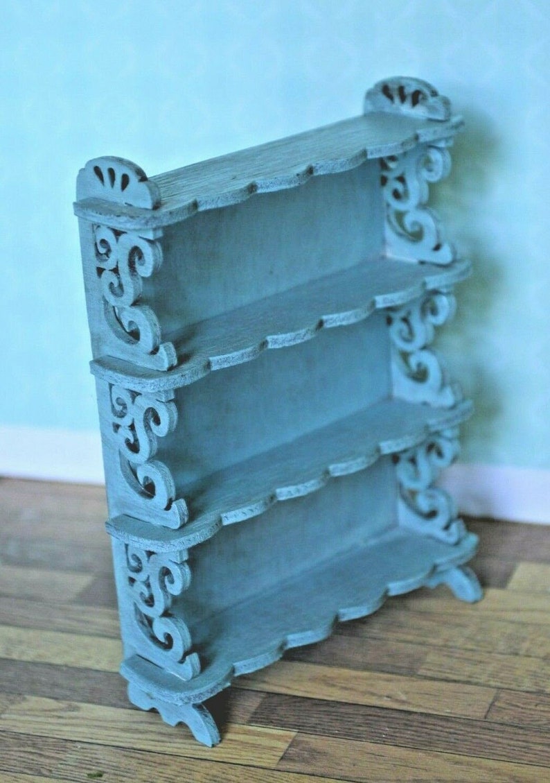 May include: A light blue wooden shelf unit with intricate scrollwork details and four shelves. The shelf unit is freestanding and has a decorative scalloped edge.