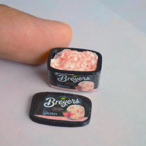 May include: A miniature black plastic container of Breyers strawberry ice cream with a matching removable lid. The container features the Breyers logo and a graphic of a scoop of strawberry ice cream with a fresh strawberry on the front label.