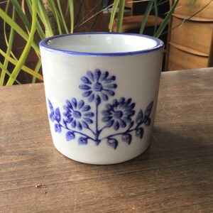 May include: White ceramic mug with a blue floral design. The mug has a blue rim and a blue floral pattern with three flowers and leaves.