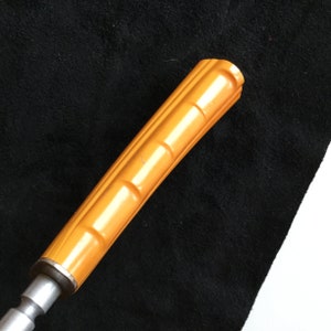 Op de afbeelding: Close-up van een vintage gereedschapshandvat. De handgreep heeft een levendige oranje kleur met een geribbeld ontwerp. De metalen basis is zilver. Het gereedschap staat tegen een zwarte achtergrond.