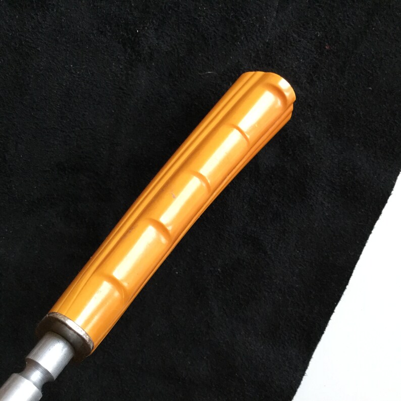 Op de afbeelding: Close-up van een vintage gereedschapshandvat. De handgreep heeft een levendige oranje kleur met een geribbeld ontwerp. De metalen basis is zilver. Het gereedschap staat tegen een zwarte achtergrond.