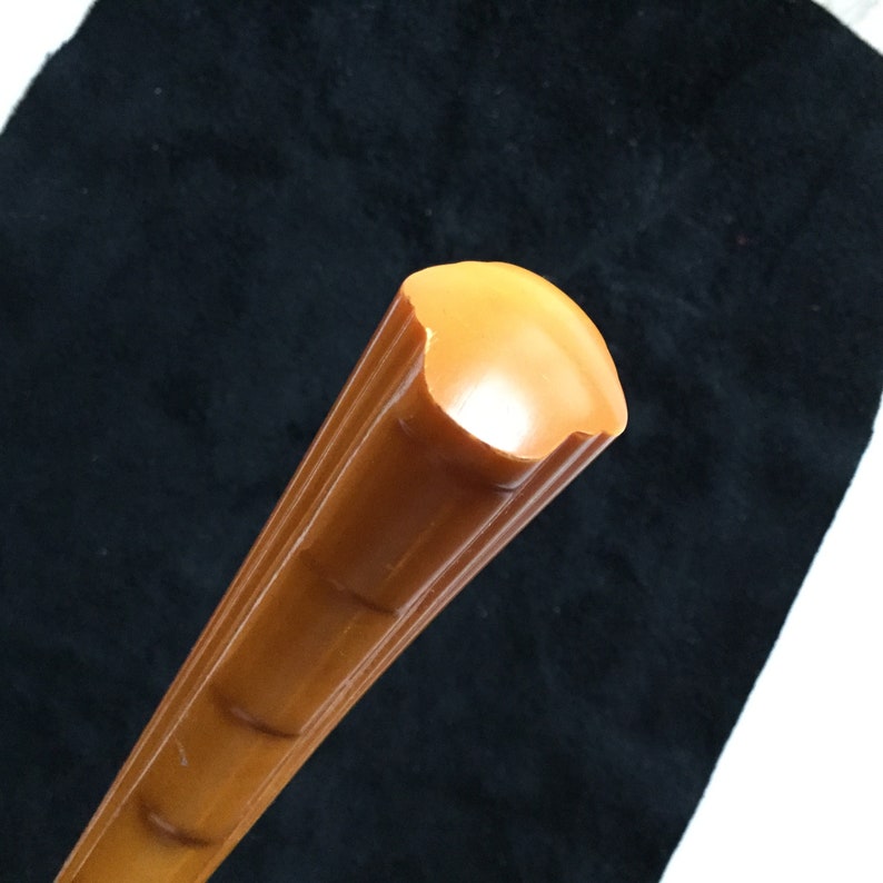 Op de afbeelding: Close-up van een bruin, cilindrisch object met een afgerond uiteinde. Het object heeft verticale groeven en een gladde, glanzende afwerking. De kleur is een warme, amberachtige tint. Het object staat tegen een donkere achtergrond.