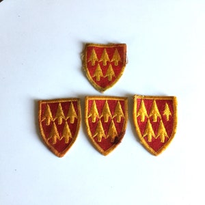 May include: A collection of five red and gold embroidered patches. Each patch features a shield shape with a gold border and six gold arrow-shaped designs. The patches are arranged on a white surface.