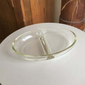 Könnte beinhalten: Eine durchsichtige Glasschüssel mit zwei ovalen Fächern. Die Schüssel steht auf einer weißen Oberfläche.