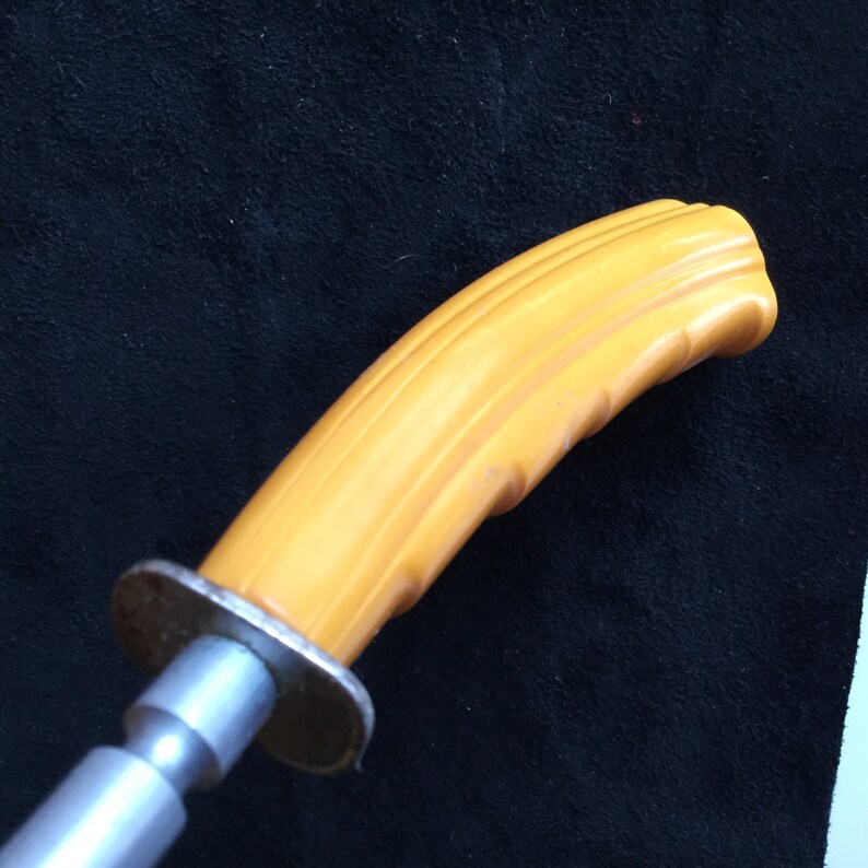 Op de afbeelding: Close-up van een meshandvat met een heldergele, geribbelde grip. De handgreep is bevestigd aan een zilveren metalen lemmet. Het mes wordt waarschijnlijk gebruikt voor keuken- of gebruiksdoeleinden.