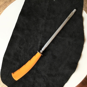 Op de afbeelding: Een messenslijpstaal met een oranje handvat en een zilveren stalen staaf. De handgreep is ergonomisch ontworpen voor een comfortabele grip. Het staal wordt gebruikt om de scherpte van messen te behouden.