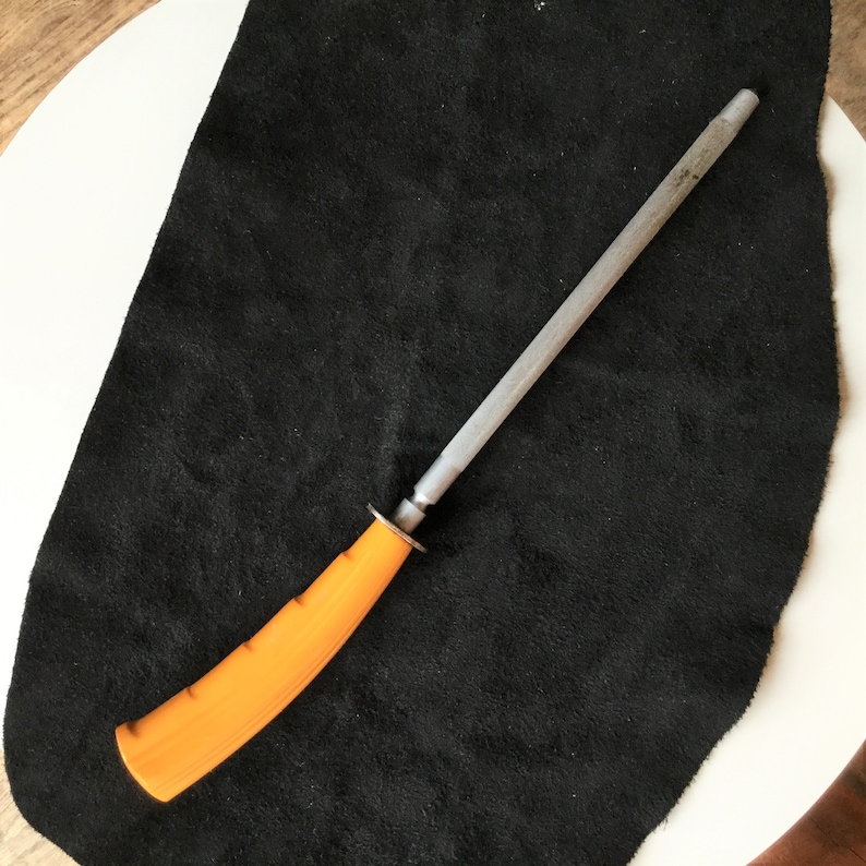 Op de afbeelding: Een messenslijpstaal met een oranje handvat en een zilveren stalen staaf. De handgreep is ergonomisch ontworpen voor een comfortabele grip. Het staal wordt gebruikt om de scherpte van messen te behouden.