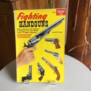 May include: A yellow book cover with the title "Fighting Handguns" and the text "History, Adventure And Romance of Handguns From The Muzzle Loader To Modern Magnums" and "Gunfighting Techniques". The cover features several different handguns, including a revolver, a pistol, and a flintlock pistol.