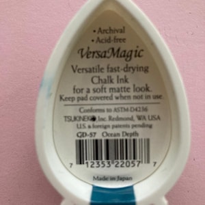 May include: White and teal VersaMagic chalk ink pad. The label reads "VersaMagic Versatile fast-drying Chalk Ink for a soft matte look." The ink pad is archival and acid-free. The product is made in Japan.