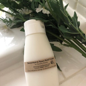 K&ouml;nnte beinhalten: Wei&szlig;e Plastikflasche mit H&auml;morrhoiden- und Analfissuren-Salbe mit einem braunen Etikett, auf dem steht: "Hemorrhoid & Fissure Relief Cream by Navoms Beauty www.navomsbeauty.com USAGE DIRECTIONS: Clean and gently massage on affected area for relief"